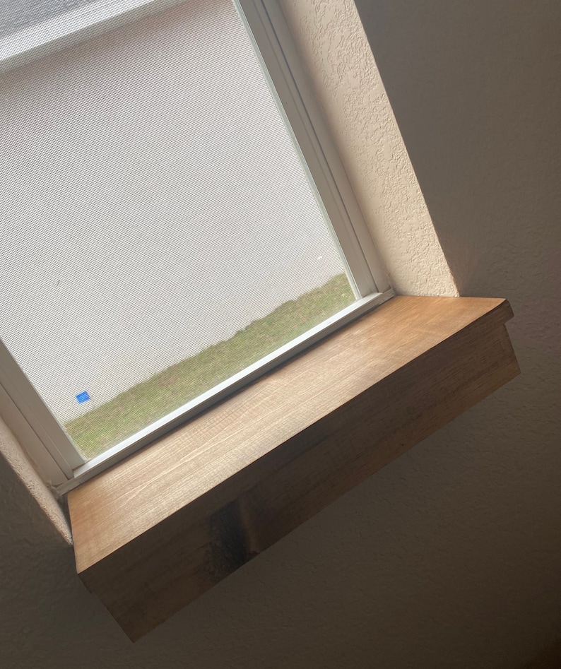 Puede incluir: Una repisa de ventana de madera con un acabado de madera natural. La repisa est&aacute; en &aacute;ngulo y montada debajo de una ventana con una pantalla blanca.