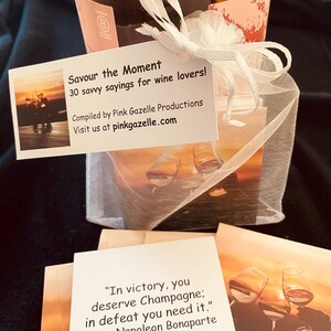 Op de afbeelding: Een wit organza zakje met trekkoord dat een kaartspel met citaten over wijn bevat. Het bijgevoegde label leest: Savour the Moment, 30 savvy sayings for wine lovers, Compiled by Pink Gazelle Productions, Visit us at pinkgazelle.com.