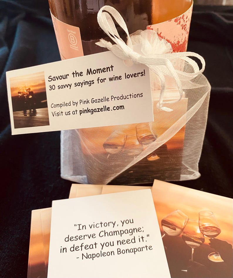 Op de afbeelding: Een wit organza zakje met trekkoord dat een kaartspel met citaten over wijn bevat. Het bijgevoegde label leest: Savour the Moment, 30 savvy sayings for wine lovers, Compiled by Pink Gazelle Productions, Visit us at pinkgazelle.com.