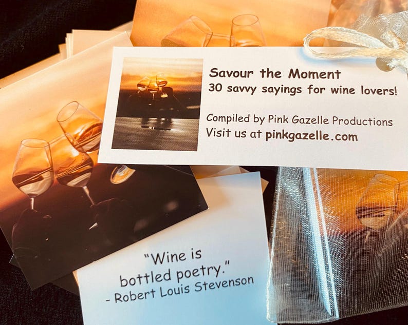 Op de afbeelding: Een set kaarten getiteld Savour the Moment 30 savvy sayings for wine lovers samengesteld door Pink Gazelle Productions. De kaarten bevatten afbeeldingen van wijnglazen bij zonsondergang en citaten zoals Wine is bottled poetry.