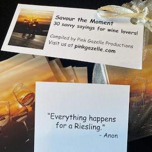Op de afbeelding: Een set kaarten getiteld Savour the Moment 30 savvy sayings for wine lovers, samengesteld door Pink Gazelle Productions. De kaarten bevatten afbeeldingen van wijnglazen en citaten zoals Everything happens for a Riesling. Verpakt in een gouden organzazakje.