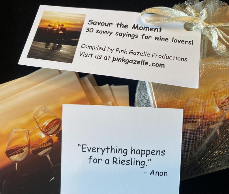 Op de afbeelding: Een set kaarten getiteld Savour the Moment 30 savvy sayings for wine lovers, samengesteld door Pink Gazelle Productions. De kaarten bevatten afbeeldingen van wijnglazen en citaten zoals Everything happens for a Riesling. Verpakt in een gouden organzazakje.