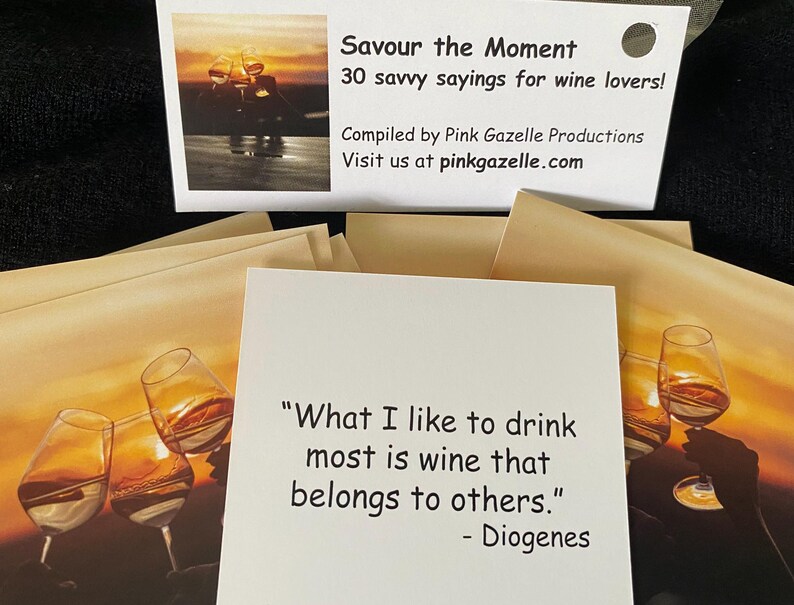 Op de afbeelding: Een set vierkante kaarten met citaten over wijn. De bovenste kaart toont de tekst: "Savour the Moment, 30 savvy sayings for wine lovers! Compiled by Pink Gazelle Productions. Visit us at pinkgazelle.com." Een andere kaart toont het citaat: "What I like to drink most is wine that belongs to others." - Diogenes, tegen een achtergrond van een zonsondergang met wijnglazen.