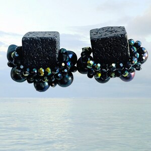 May include: A pair of black earrings with a square-shaped black stone base and a cluster of iridescent black beads.