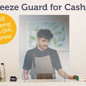 Può includere: Una protezione trasparente contro gli starnuti per un cassiere, con la scritta "Sneeze Guard for Cashier" in alto. La protezione è posizionata di fronte a una persona che indossa un grembiule. Una bilancia, un terminale di pagamento e altri oggetti sono sul bancone.