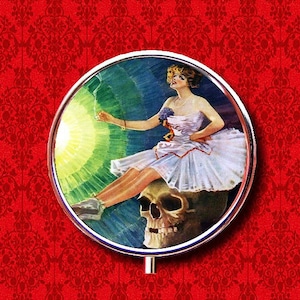 Puede incluir: Un espejo compacto de estilo vintage con un marco plateado. La superficie del espejo muestra a una mujer con un vestido blanco sentada sobre un cráneo. El fondo es un degradado verde y azul con una luz brillante que brilla detrás de la mujer.