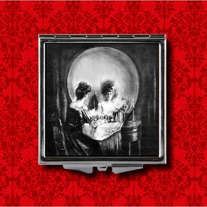 May include: A black and white compact mirror with a skull image. The skull is formed by two women looking at each other in a mirror.