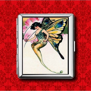 May include: A silver cigarette case with a vintage illustration of a fairy with butterfly wings. The fairy is in a flowing gown, with a pink flower. The background is red with a pattern.