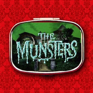 Puede incluir: Un compacto plateado con una imagen de fondo verde de una casa con el texto "The Munsters" en letras azules que gotean.