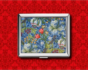 May include: A silver cigarette case with a floral pattern. The case has a blue background with a design of white, green, and red flowers and leaves. The rectangular case is set against a red background.