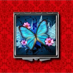 Puede incluir: Un espejo compacto con una mariposa azul y flores rosas sobre un fondo abstracto azul y blanco.