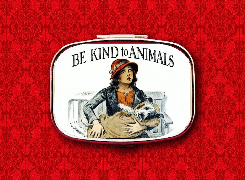 May include: A white metal compact with a red and white image of a girl holding a dog. The compact has the text "BE KIND to ANIMALS" printed on it.