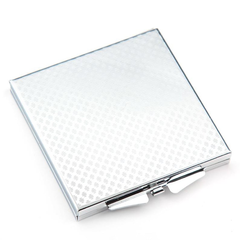 May include: A silver compact mirror with a textured surface and a hinged lid.