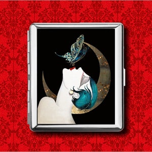 May include: A silver cigarette case featuring an art deco illustration of a woman with teal hair and a butterfly. The woman is looking up at the butterfly against a black background with a gold crescent moon.