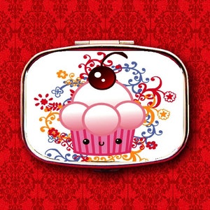 May include: A white compact mirror with a colorful floral design and a pink cupcake with a red cherry on top. The cupcake has a smiling face.