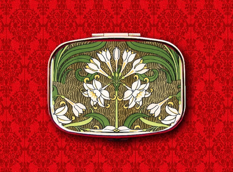May include: A vintage-style compact with a floral design. The compact features a silver-toned frame and a green and brown floral pattern with white flowers.