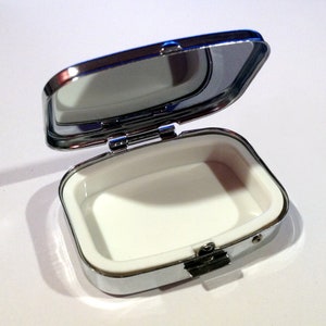 May include: A small, silver, rectangular box with a hinged lid and a mirror inside. The box is open and the interior is white.