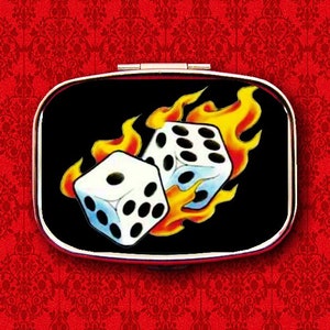 Puede incluir: Un compacto plateado con fondo negro y un gráfico de dos dados en llamas. Los dados son blancos con puntos negros.