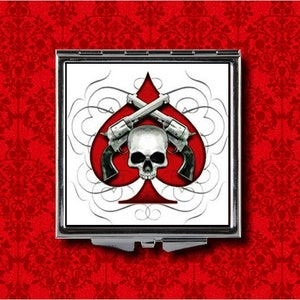 May include: A compact mirror with a white background and a red ace of spades with two crossed pistols and a skull in the center.