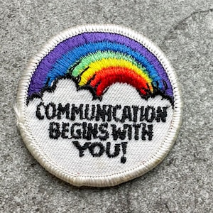May include: Embroidered patch with a rainbow design above white clouds. The patch has a white border and the text "COMMUNICATION BEGINS WITH YOU!" in black. The rainbow features purple, blue, green, yellow, and red colors.