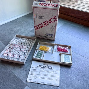 May include: A board game set with a box and game pieces. The box is white with red and black text that reads "SEQUENCE". The game board is rectangular with card images. Includes cards and colored chips.