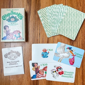 May include: A vintage Cabbage Patch Kids card game box with a green and white design. The box features a picture of three Cabbage Patch Kids dolls. The text on the box reads "Cabbage Patch Kids Card Game Make New Friends 3 Games in 1".