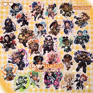 May include: A selection of colourful pixel art stickers depicting characters from the video game Overwatch. The stickers are arranged on a yellow and white checked background. The text "Overwatch pixel stickers" is visible.