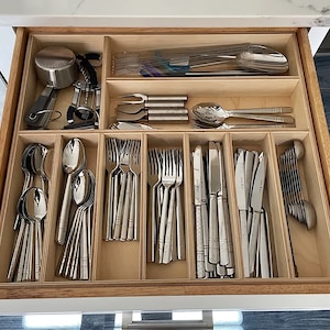 May include: A wooden drawer organiser with multiple compartments for storing cutlery. The organiser is filled with various types of cutlery, including spoons, forks, and knives.
