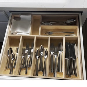 May include: A wooden cutlery organizer with multiple compartments for storing silverware. The organizer is filled with various spoons, forks, and knives.