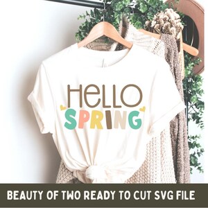 May include: A white t-shirt with the text "HELLO SPRING" in brown, yellow, pink, and blue letters. The letters are outlined in black and have small hearts on either side of the word "SPRING".