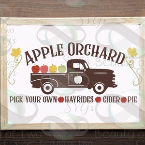 May include: A white sign with brown lettering that reads "APPLE ORCHARD" with a silhouette of a brown pickup truck with red apples in the bed. The text below the truck reads "PICK YOUR OWN HAYRIDES CIDER PIE".