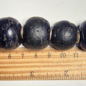 May include: Close-up of a strand of large, dark blue beads with silver-colored spacers. The beads are roughly 1 inch in diameter. A wooden ruler with inch markings is in the foreground, providing scale.