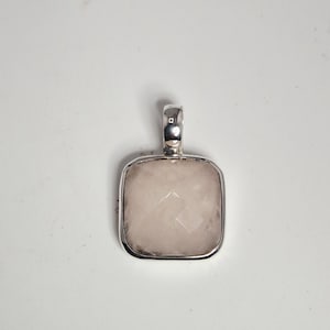 Peut inclure: Un pendentif carré avec une pierre précieuse rose clair à facettes, sertie dans un cadre en métal argenté. Le pendentif a une boucle en haut pour une chaîne. La pierre a une qualité subtile et translucide.