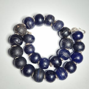 May include: A necklace composed of dark blue and black beads. The beads are round and strung together with silver-colored metal. The necklace is displayed on a white background.
