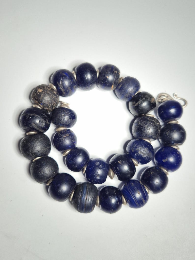 May include: A necklace composed of dark blue and black beads. The beads are round and strung together with silver-colored metal. The necklace is displayed on a white background.