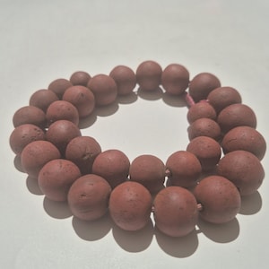 May include: A necklace made of reddish-brown, spherical beads. The beads are strung together, forming a circular shape. The beads have a textured surface and are evenly spaced along the string.