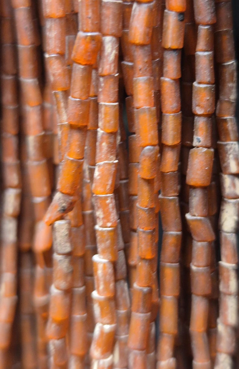 May include: Close-up of strands of amber-colored beads. The beads are cylindrical with rounded edges, creating a textured surface. The color varies from light to dark amber, with some beads appearing more opaque than others. The beads are strung together, forming vertical lines.