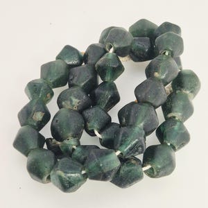 Könnte beinhalten: Strang aus dunkelgrünen, facettierten Glasperlen. Die Perlen sind unregelmäßig geformt und leicht durchscheinend, auf einer weißen Schnur aufgereiht. Die Perlen haben ein Vintage- oder antikes Aussehen.