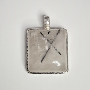 May include: Square pendant with a clear, textured center and a silver-colored frame. The pendant features a black, intersecting line design. The bail is also silver-colored.