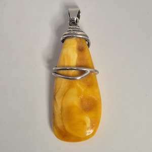 May include: A teardrop-shaped pendant featuring a polished amber stone with natural patterns. The amber is encased in a silver wire setting, with a loop at the top for a chain. The pendant is a warm, golden color.