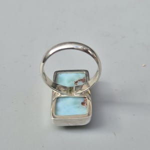 May include: A silver ring featuring two rectangular, light blue gemstones with brown inclusions. The ring's band is a simple, polished silver. The gemstones are set in a silver bezel.