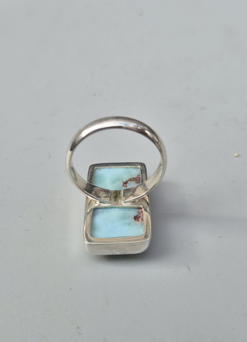 May include: A silver ring featuring two rectangular, light blue gemstones with brown inclusions. The ring's band is a simple, polished silver. The gemstones are set in a silver bezel.