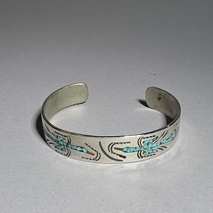 Op de afbeelding: Zilveren manchetarmband met turkoois en rode inlegwerk libellenontwerpen. Het open manchetontwerp maakt het gemakkelijk om te dragen. De armband is een uniek sieraad.