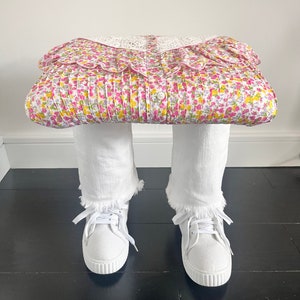 May include: A white floral print blouse with a white lace collar and white frayed denim jeans with white sneakers.