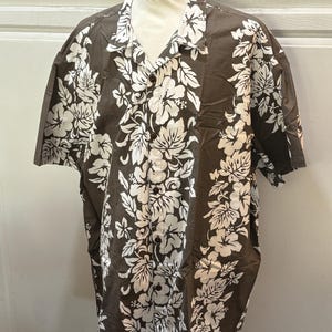 May include: A brown short-sleeved button-up shirt with a white floral print. The shirt has a classic collar and a button-up front.