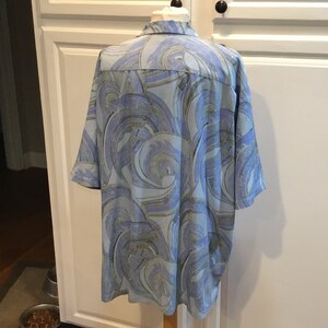 May include: A blue short-sleeved shirt with a swirling abstract pattern in shades of blue, green, and gold.