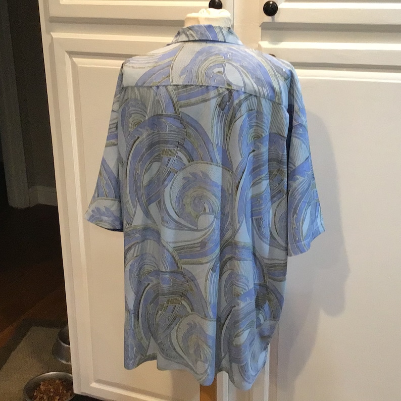 May include: A blue short-sleeved shirt with a swirling abstract pattern in shades of blue, green, and gold.