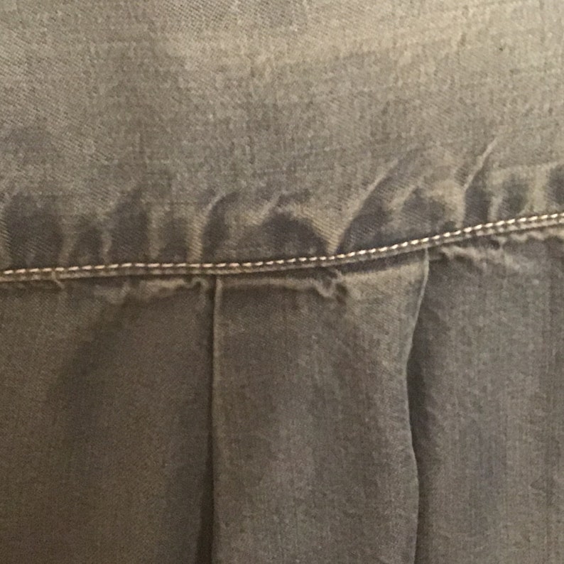 May include: Close-up of a dark blue denim skirt with a single seam running across the top.