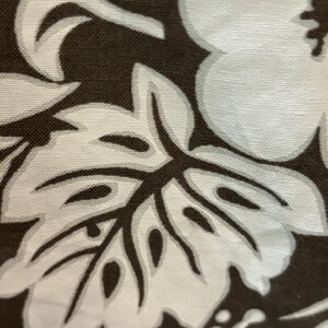 May include: A close-up of a brown fabric with a white floral pattern. The pattern features large hibiscus flowers and leaves.