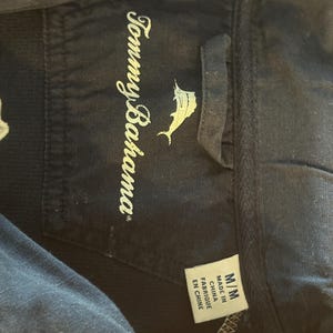 May include: Close-up of a navy blue garment tag with the Tommy Bahama logo and text. The tag also includes size information and the text "Made in China / Fabriqu&eacute; en Chine".
